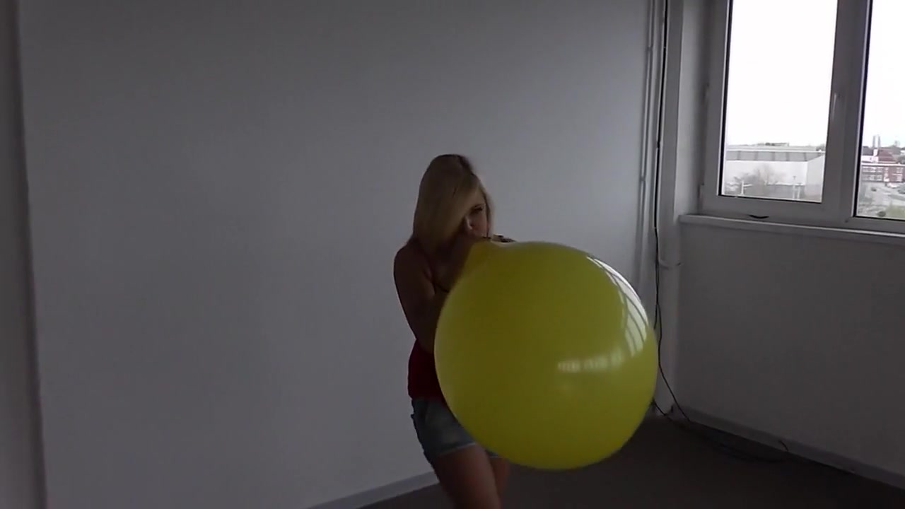 Milena blows to pop big yellow balloon